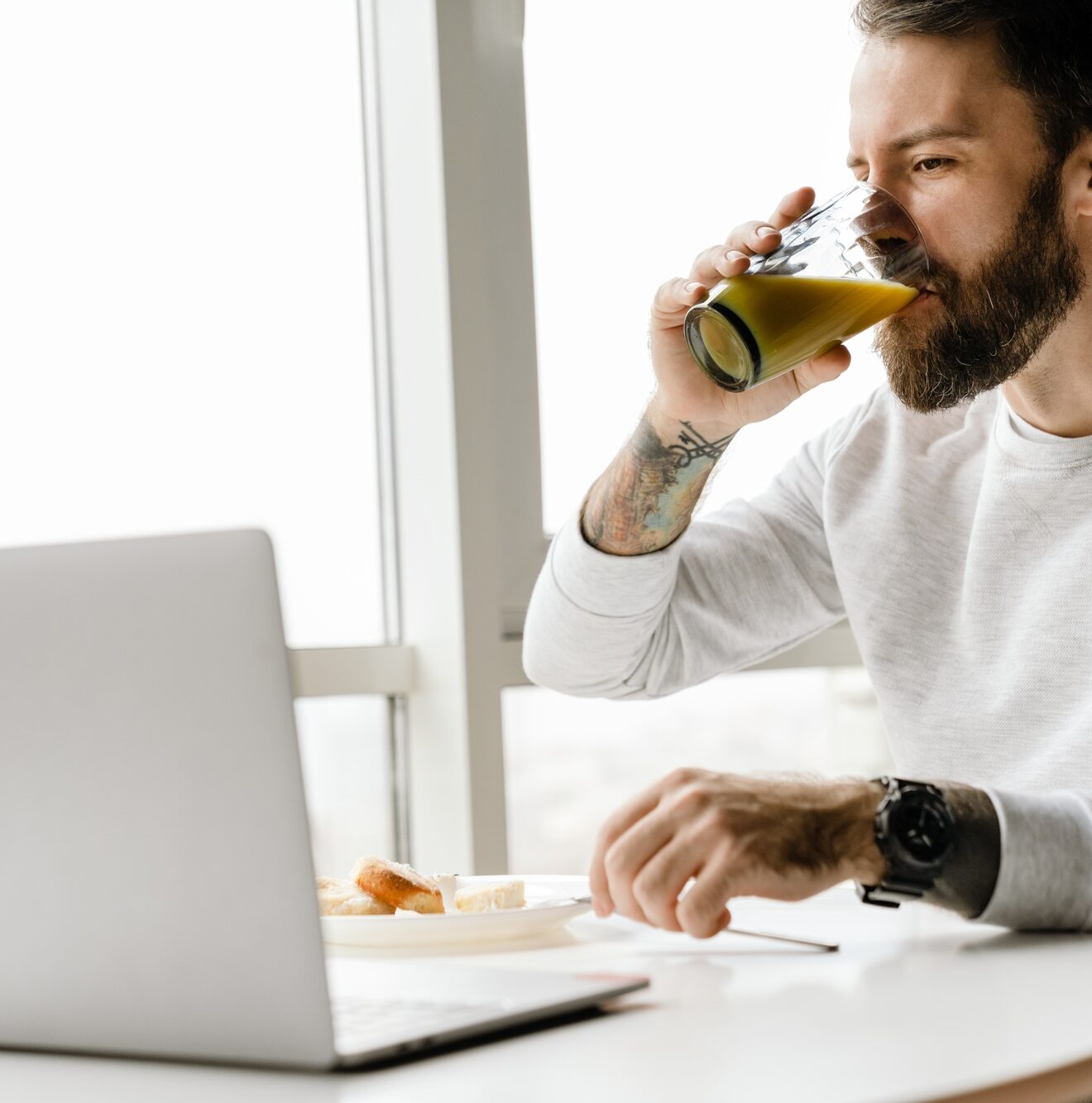 Bearded european man working with laptop while having breakfast